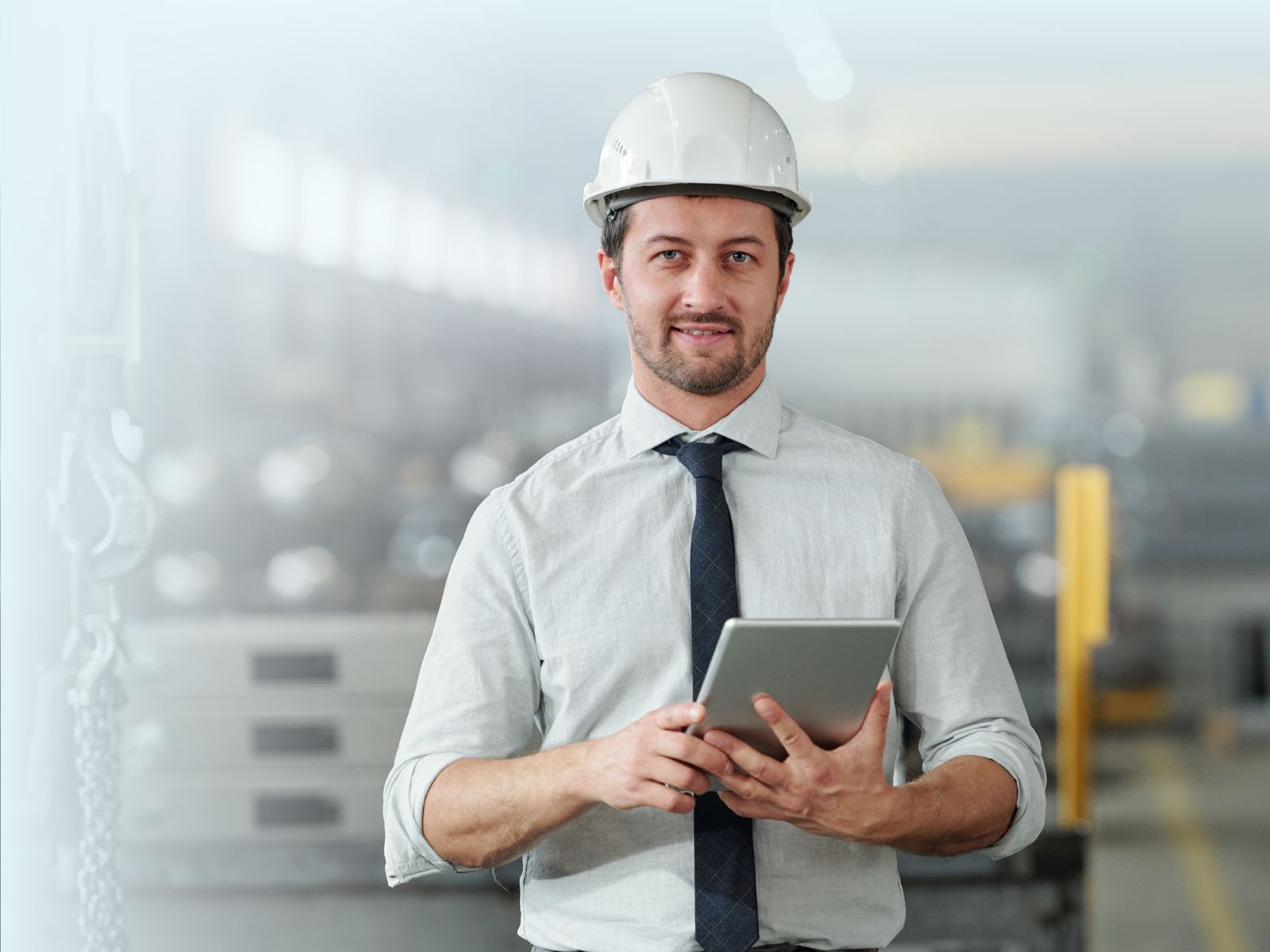 Ingeniero de manufactura o supervisor con casco de seguridad blanco, usando una tablet para gestionar la operación en el piso de una fábrica industrial.