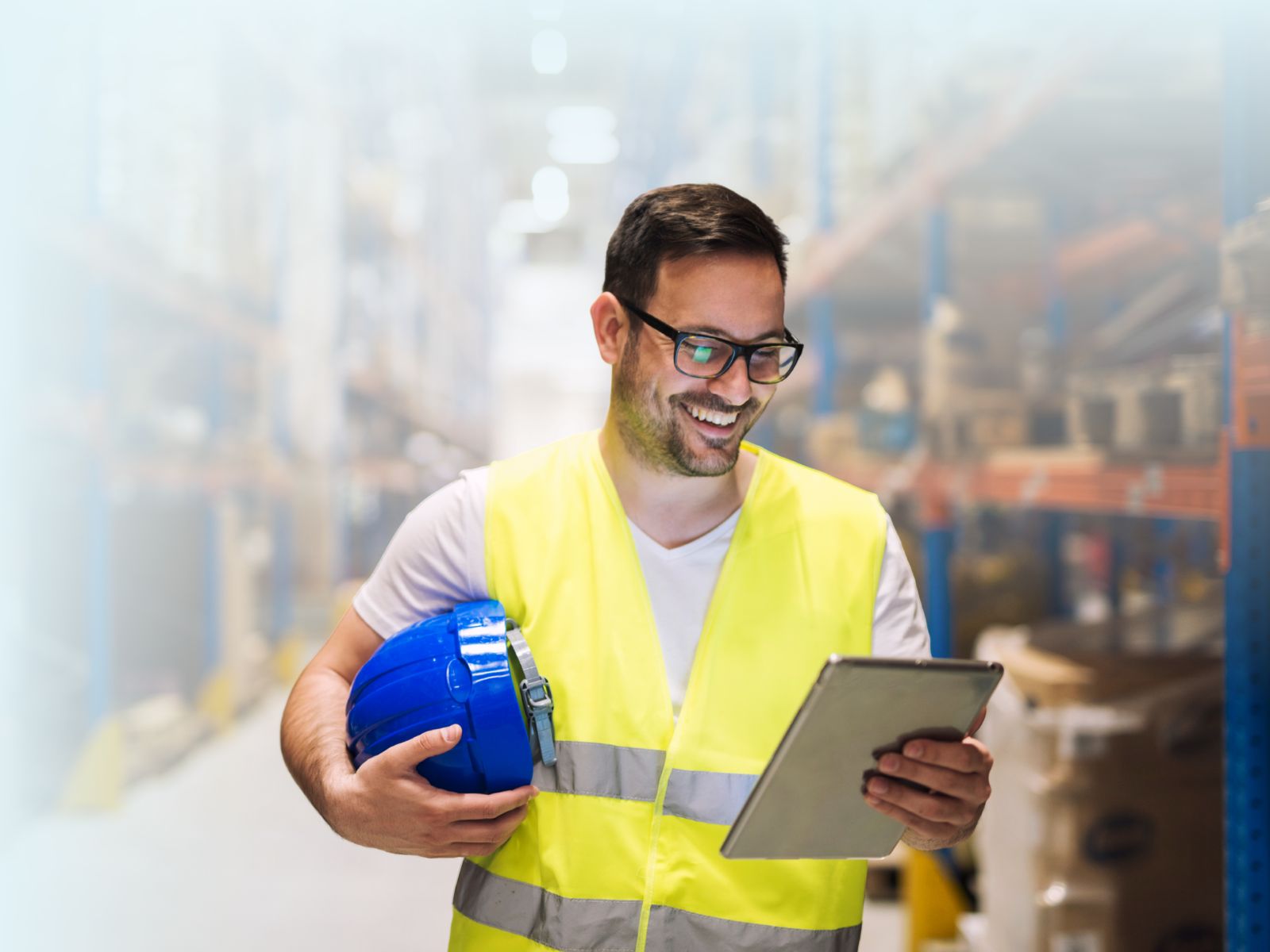 Supervisor o almacenista sonriendo con chaleco de seguridad reflectante naranja y brazos cruzados, en un centro de distribución o almacén.